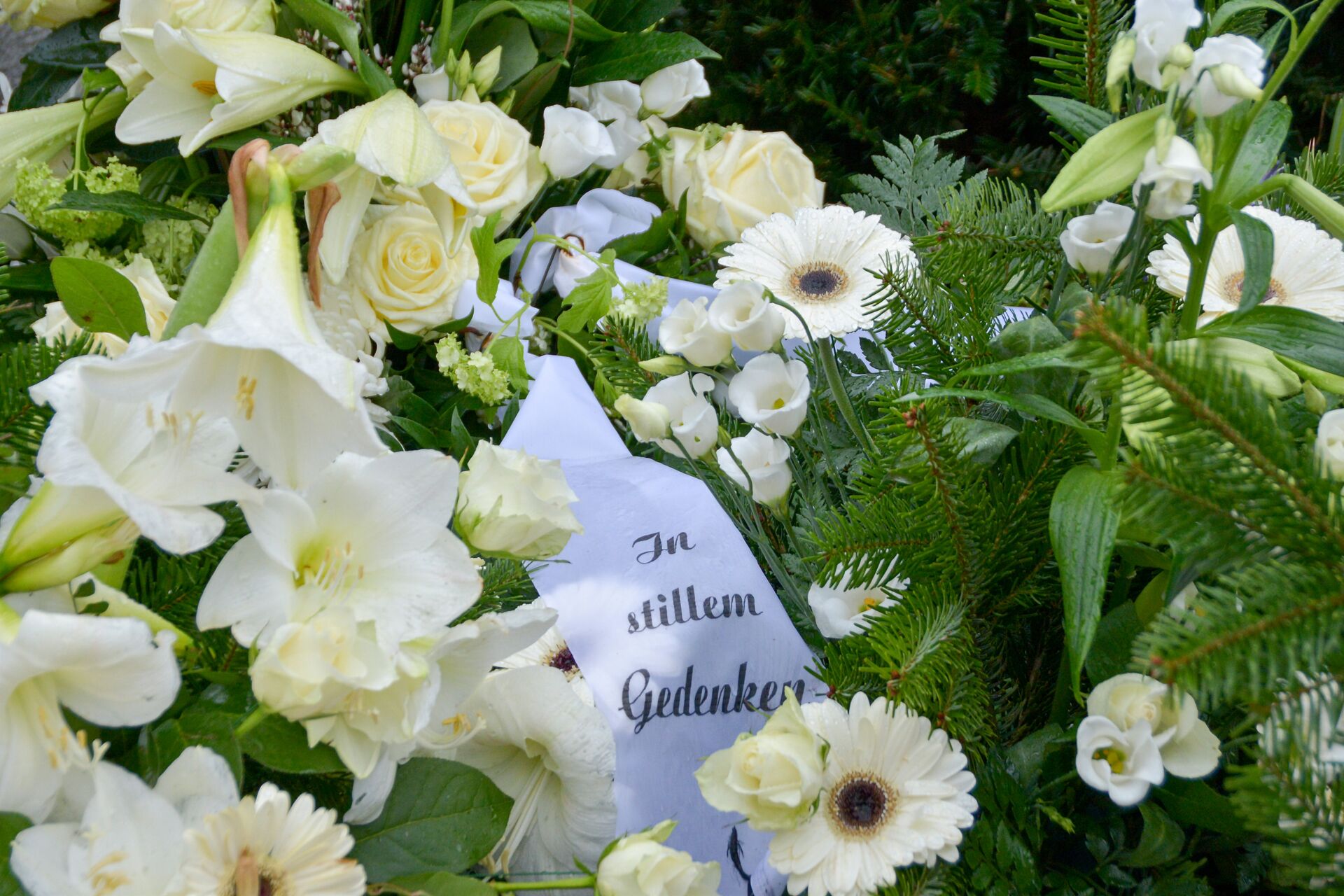 Bestattung Eva-Maria Hinz - Trauerfloristik Weißes Trauergesteck mit Lilien, Rosen, Gerbera und Schleife "In stillem Gedenken"; würdevolle Trauerfloristik von Bestattung Hinz.